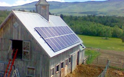 Solar panels on grey barn metal roof with animal paddock in front and Green Mountains in background