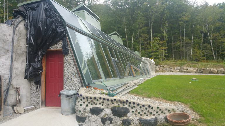 Solar panels above greenhouse section of Earthship house with green lawn in front